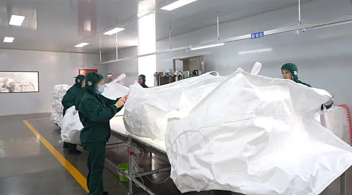 Workers inspecting seams and stitches of large white FIBC bags in a clean workshop.
